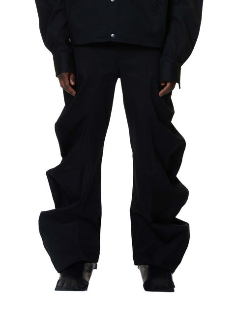 A person standing wearing deflated signature black denim trousers with an oversized style.