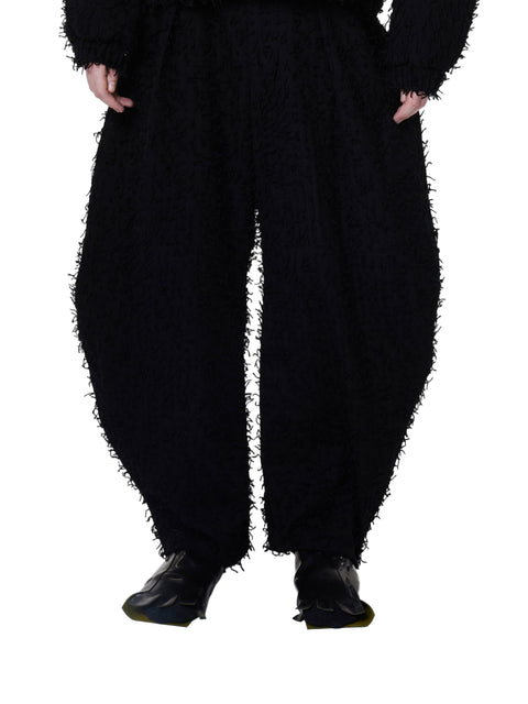 A person standing wearing wide-leg black trousers with a fuzzy texture, designed to be worn loose, with the trousers tapering at the ankle.