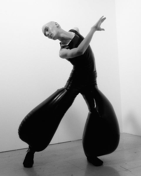 Model wearing black inflatable latex trousers and latex bodysuit by HARRI London, arms extended in a wide stance showing the full inflated silhouette, photographed by Kaj Lehner