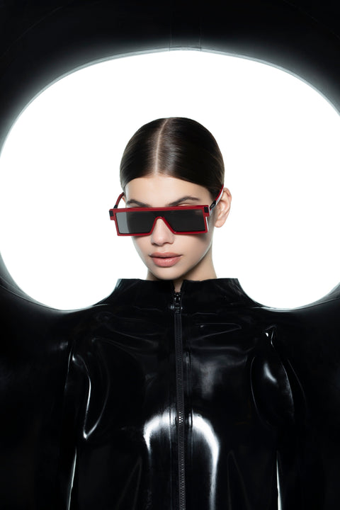 Female model wearing VAVA x HARRI London CL0031 red-frame rectangular sunglasses and black HARRI London latex zip-up jacket, circular backlit backdrop