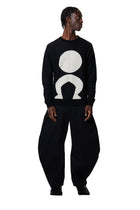 Person wearing a black sweater with a white logo and matching pants on a white background