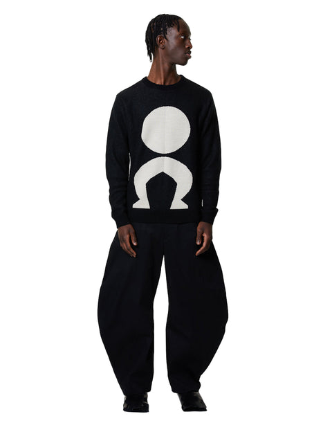 Person wearing a black sweater with a white logo and matching pants on a white background