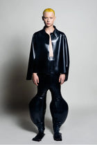Model wearing HARRI EXCLUSIVE black inflatable latex trousers with matching latex shirt against gray background