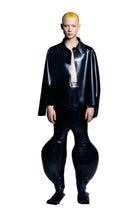 A person standing wearing black inflatable trousers with an alien-like silhouette, including extra-large legs.