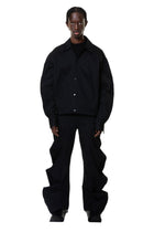 A person standing wearing deflated signature black denim trousers with an oversized style.