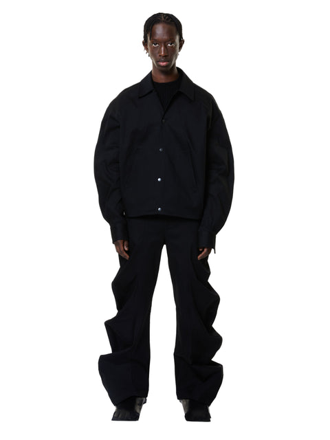 A person standing wearing deflated signature black denim trousers with an oversized style.