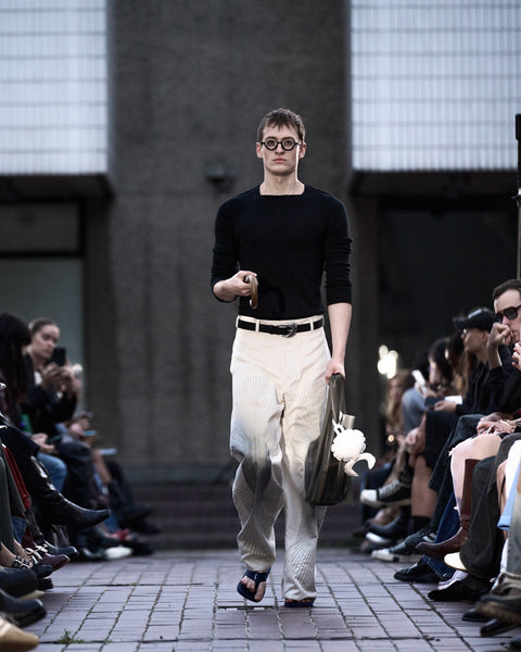 HARRI Black knit jumper paired with embroidered white trousers and a green tote bag