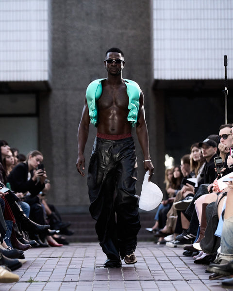 HARRI Jade green gilet paired with black leather trousers and a white baseball cap