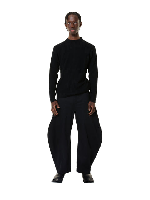 A person standing wearing a black long-sleeve top and black wide-leg trousers.