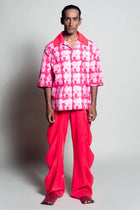 Person wearing a pink and white patterned shirt with bright pink pants on a white background