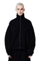 A male model wearing a black, fuzzy textured jacket with a standing collar and a front zip closure.