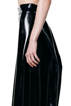 HARRI black pleated skirt with a glossy finish shown from the side on a model