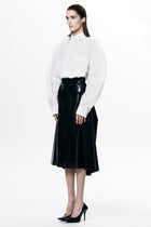 Woman wearing a HARRI black pleated skirt paired with a white long sleeve shirt and black heels