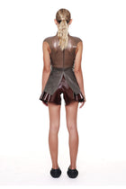 Woman wearing brown high waist flared shorts from HARRI with a unique sheer top and black slip-on shoes