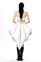Back view of a model wearing a white HARRI Tube Top paired with an avant-garde white skirt and black boots